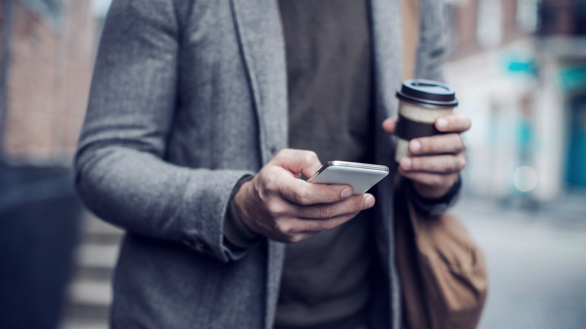 Close-up of man using phone and holding coffee