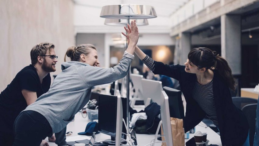Group of happy people giving each other high five in office space