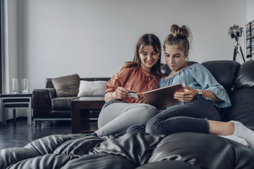 Two girls sitting in couch with tablet and credit card