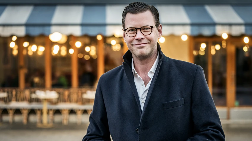 Man in glasses standing outdoors in a coat.