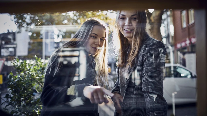 two-young-women-looking-through-shop-window
