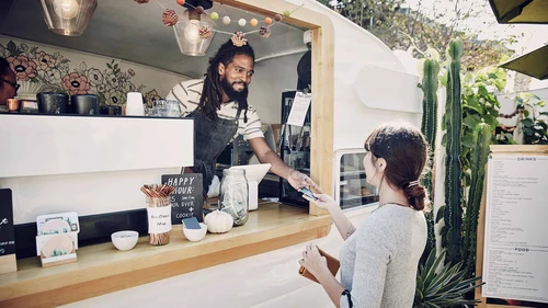 Man in food truck smiling and receiving card payment from female customer