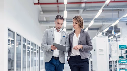 Man and woman walking down a hallway in a warehouse and looking at a tablet