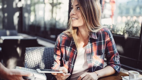 Young woman performing a payment with her mobile phone in an outside restaurant