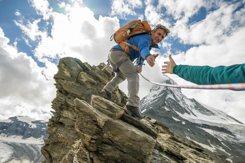 Climber on mountain reaching out to help another climber