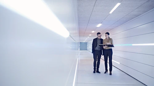 businesswoman-and-man-reading-file-in-office-corridor
