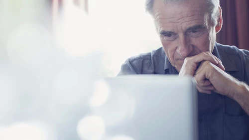 Senior man with hands clasped using laptop