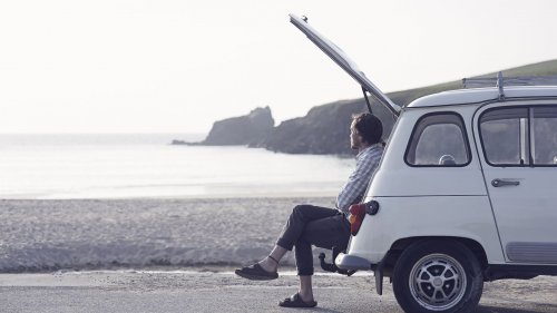 Man sitting in boot of retro car looking out on beach