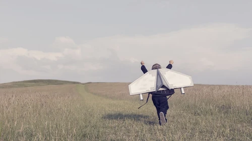 Boy wearing jetpack and running on field with arms in the air