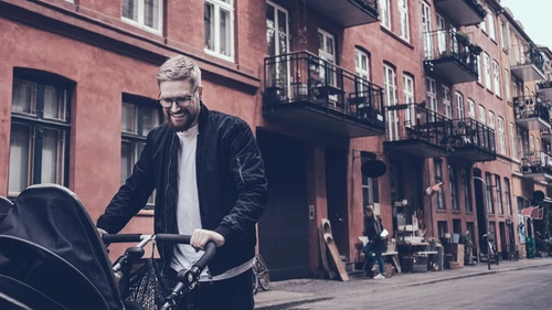 Happy man pushing baby carriage on the street in city