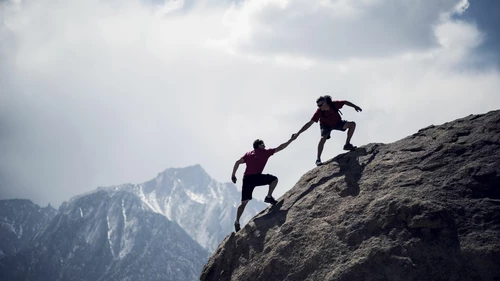 One climber helping another to the summit of a giant boulder