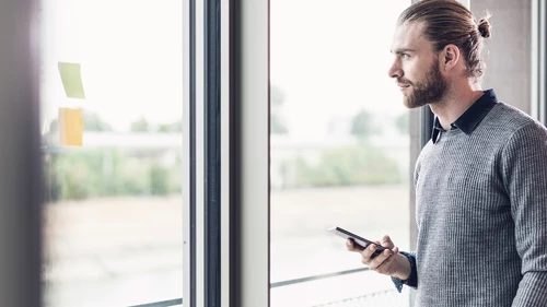 Young businessman with cell phone looking out of window