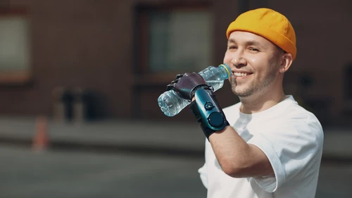 Young disabled man hold and drink bottled pure water with artificial prosthetic hand