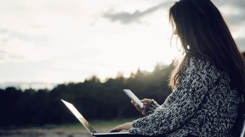 Woman with laptop text messaging while sitting at beach
