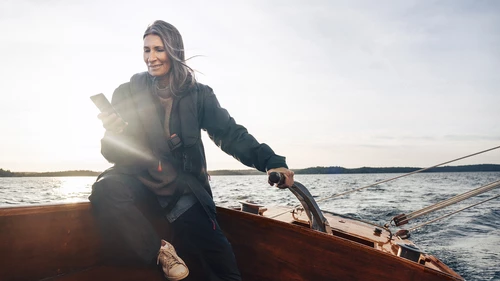 women in sailboat steering and glancing at mobile