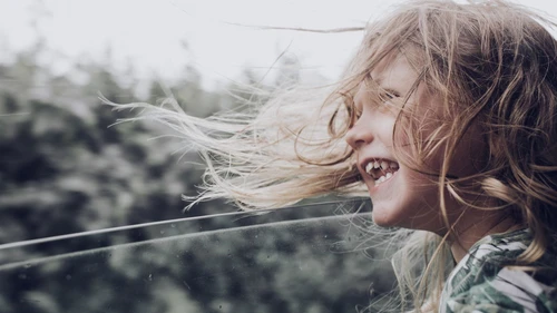happy girl sitting in car with window open and her hair blows in the wind