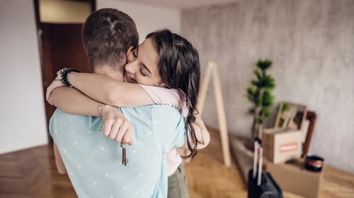 Nuori mies ja nainen halaavat huoneessa, jossa on muuttolaatikoita. Naisella on avain kädessään.