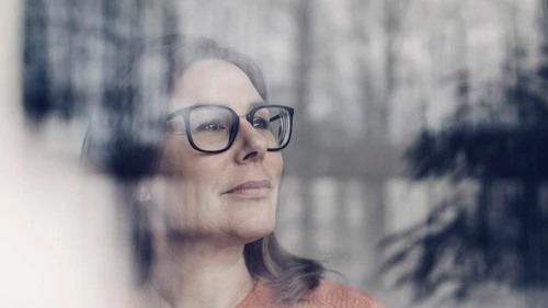 Closeup of thoughtful businesswoman wearing eyeglasses seen through window