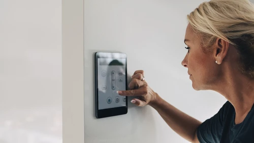Vaaleahiuksinne nainen säätää huoneen seinällä olevaa digitaalista termostaattia.