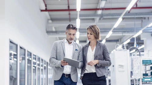 Businesswoman and businessman with tablet walking and talking in a modern factory