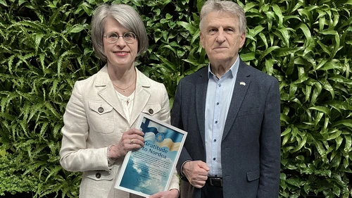 two people standing in front of a green wall holding an award