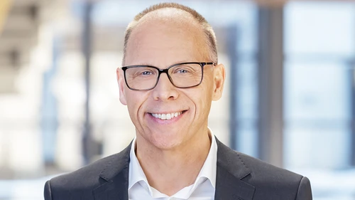 Man in glasses looks into the camera smiling.