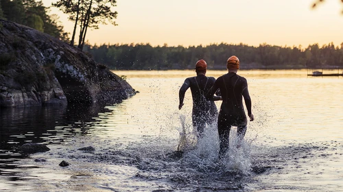 Two people in wet suits running into the water.