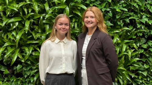 Jade Halme and Sara Nylund standing in front of a green wall