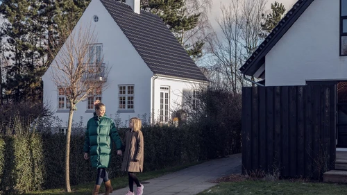 Talvivaatteisiin pukeutuneet äiti ja tytär kävelevät valkoisten omakotitalojen edessä toisiinsa katsoen.