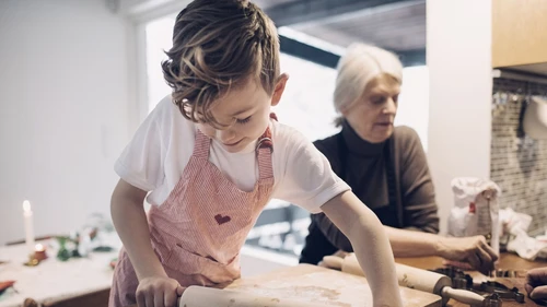 Pieni poika kaulitsee taikinaa ja hänen takanaan on iäkäs nainen asettelemassa pipareita
