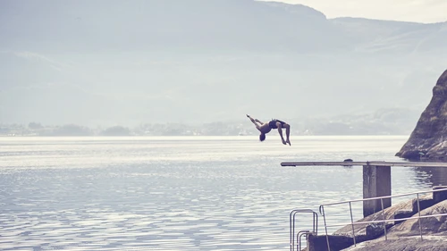 Man jumping off trampoline into a fjord.