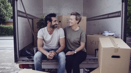 Couple looking at each other while sitting by cardboard boxes in van
