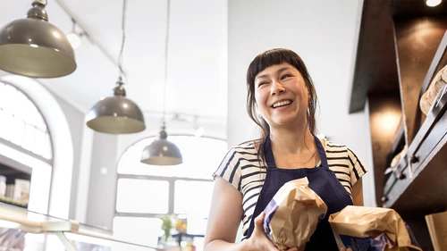 female-baker-caring-two-bags-of-bread-at-a-bakery.