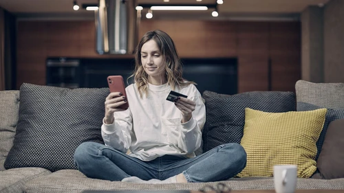 Young woman sitting on a sofa and holding a credit card