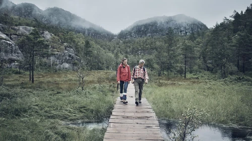 Two hikers passing through a brook on wooden bridge