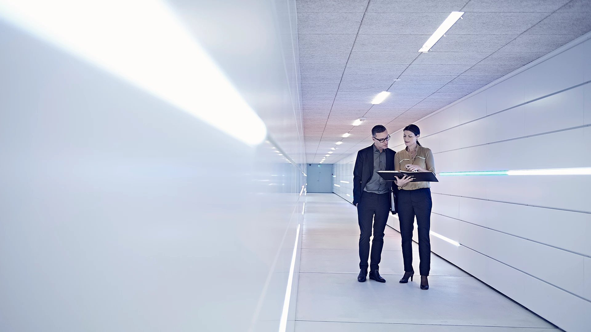 businesswoman-and-man-reading-file-in-office-corridor