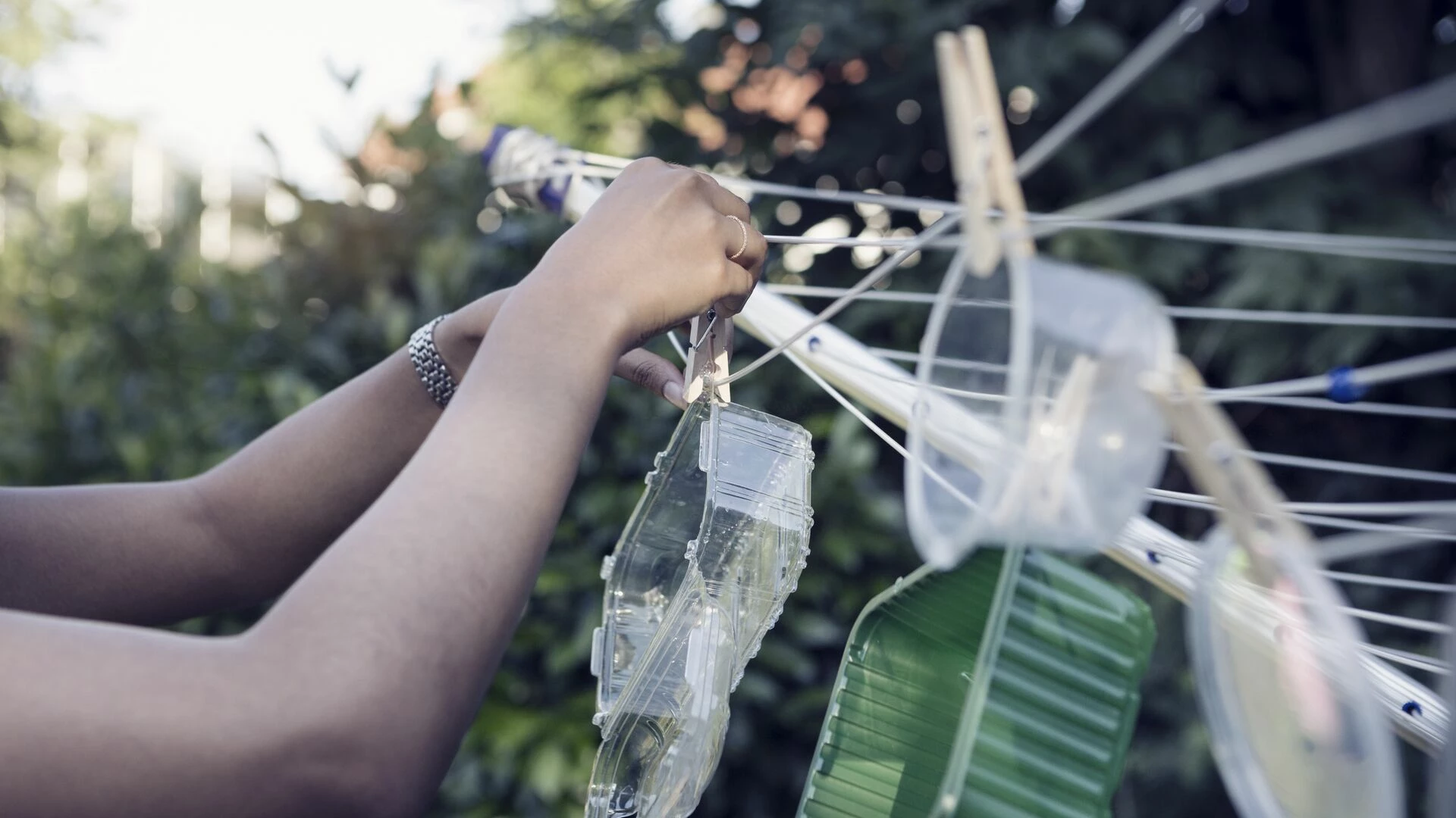 woman-hanging-washed-plastic-containers-onto-a-clothesline