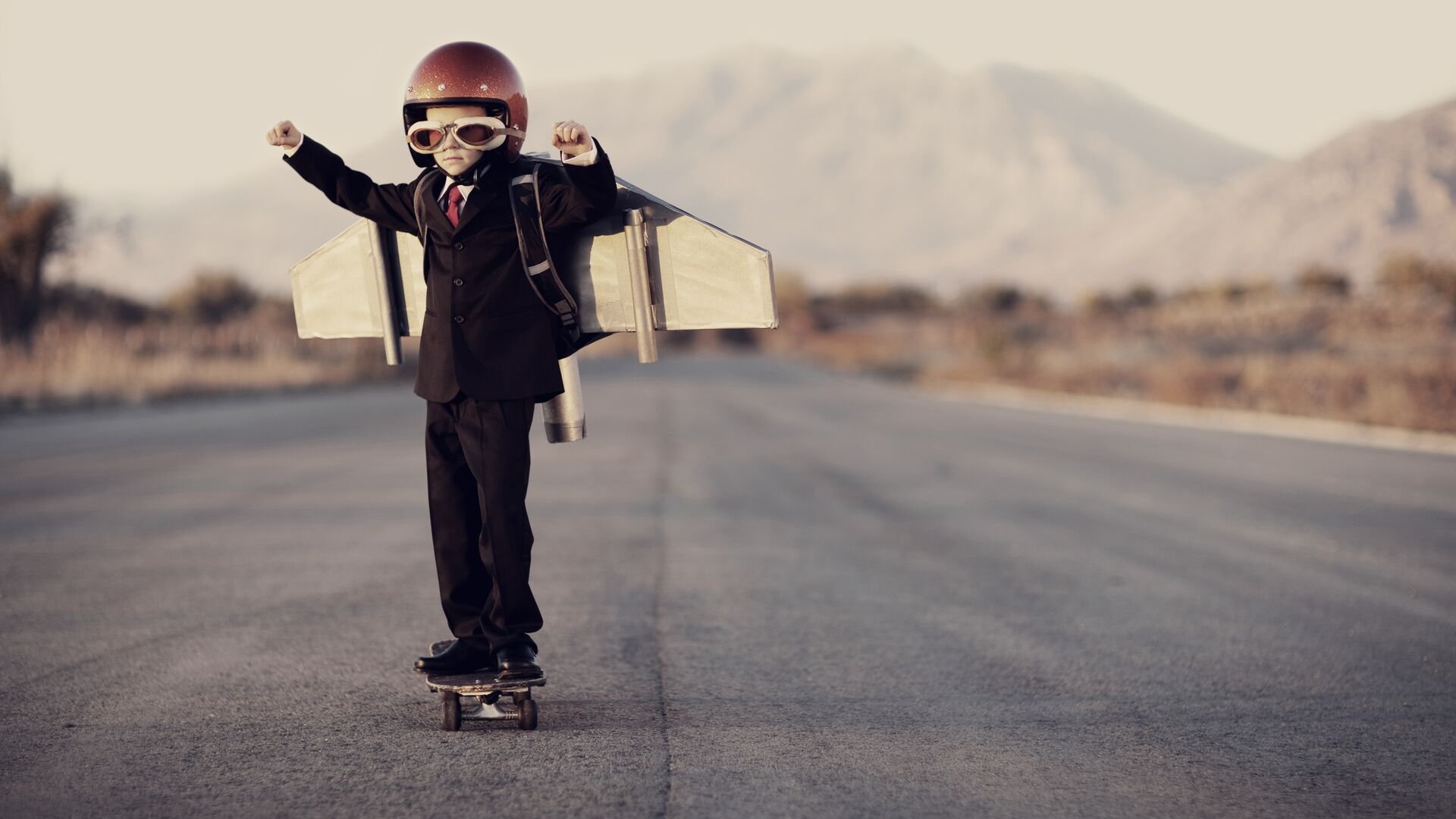 Young boy wearing business suit and jet pack on skateboard