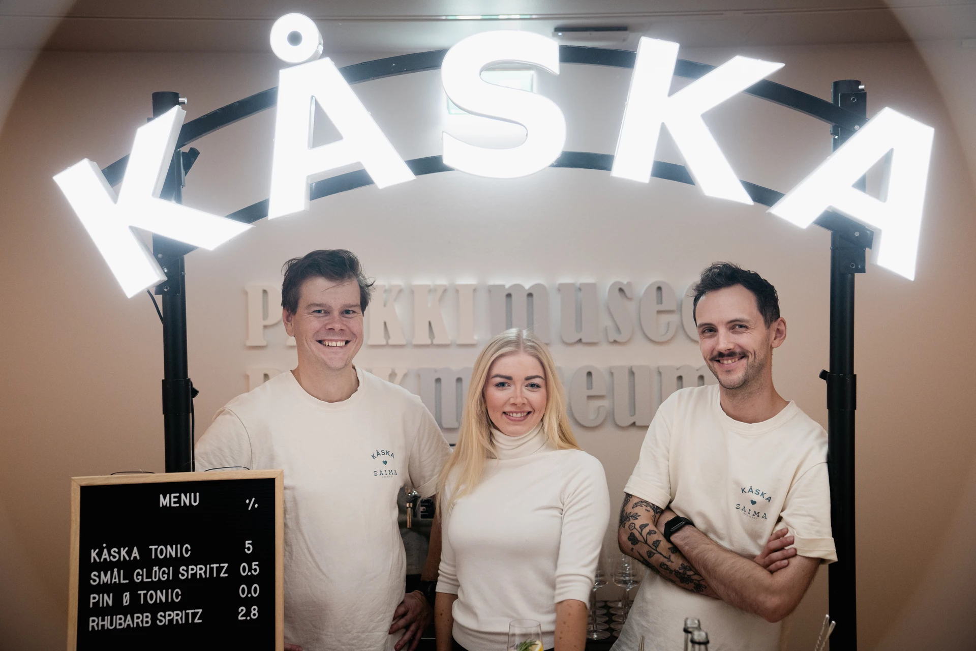 Two men and a woman smiling under a logo frame