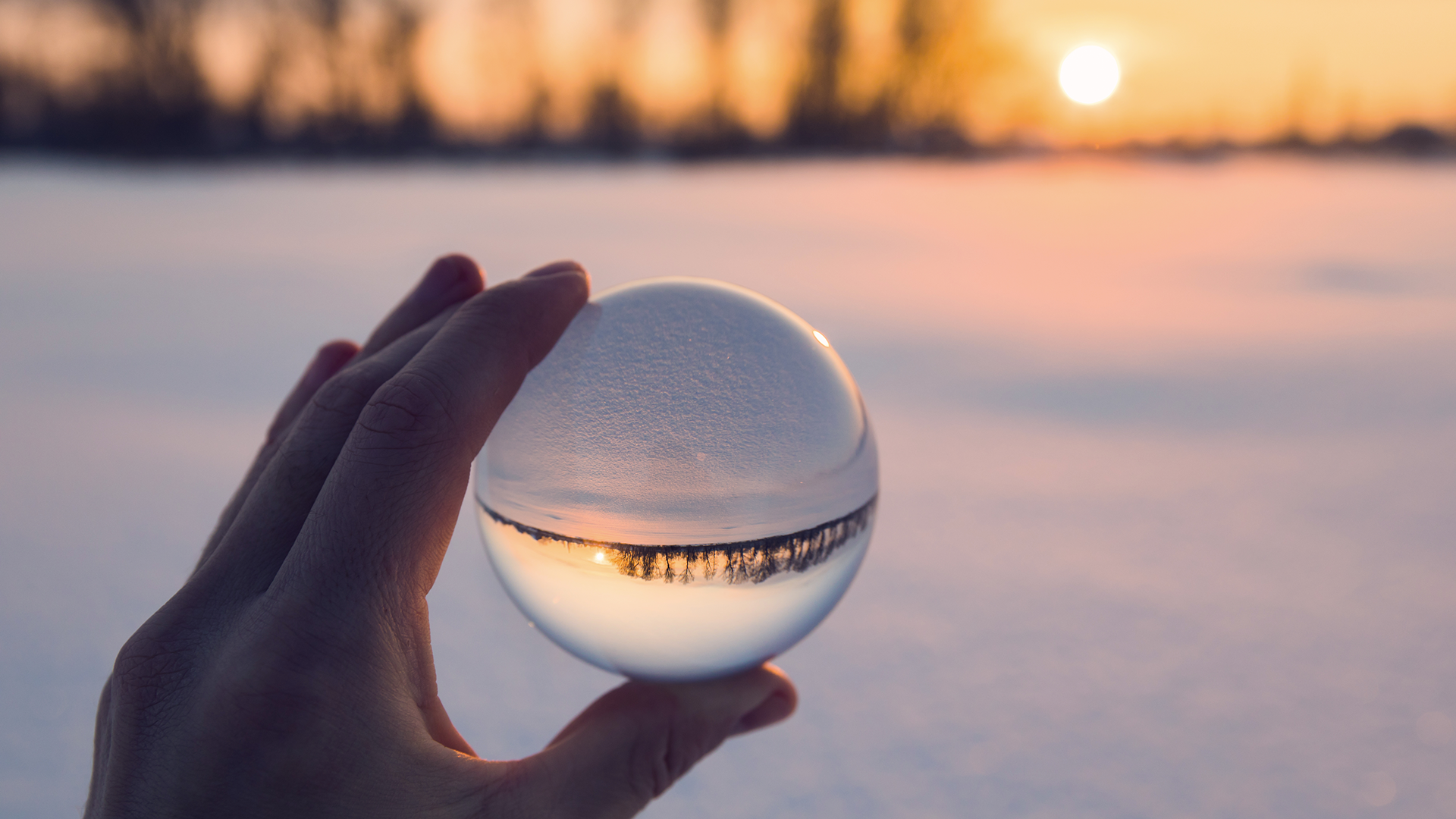 Hand holding a crystal ball with snowy sunset in the background