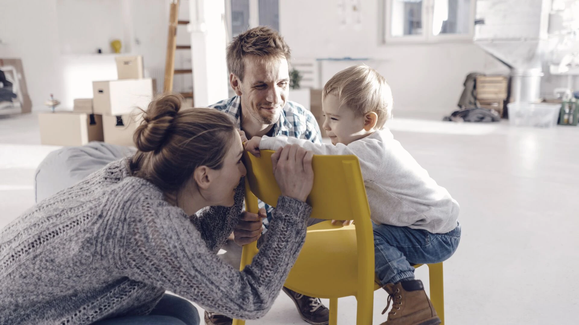 Nainen, mies ja pieni lapsi ovat iloisen näköisiä kodissa, jossa on muuttolaatikoita