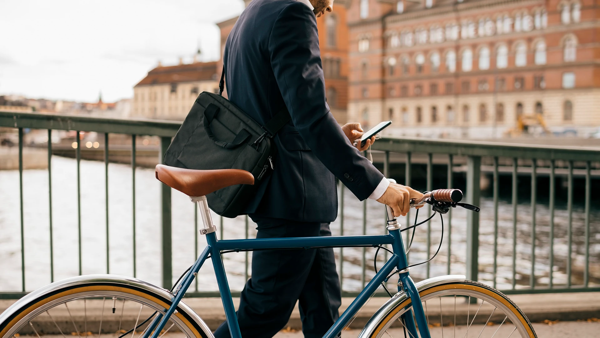 Midsection of businessman using smart phone while walking with bicycle on bridge in city