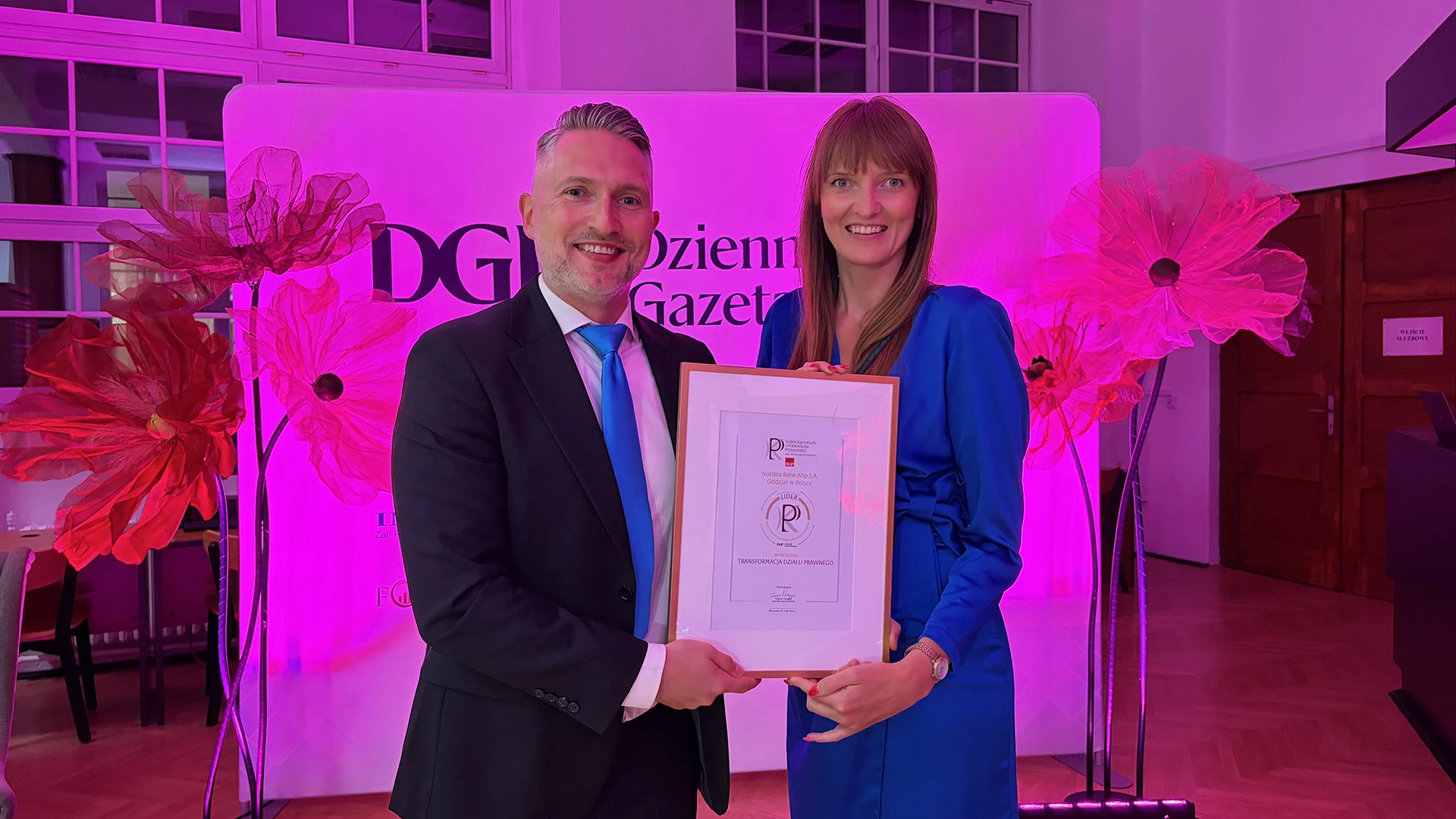 People holding a diploma in pink light.