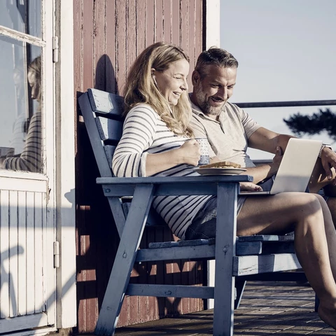 Smiling couple using laptop while having breakfast at porch