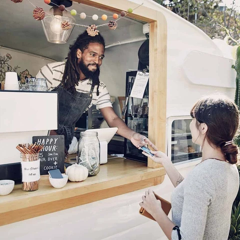 Man in food truck smiling and receiving card payment from female customer