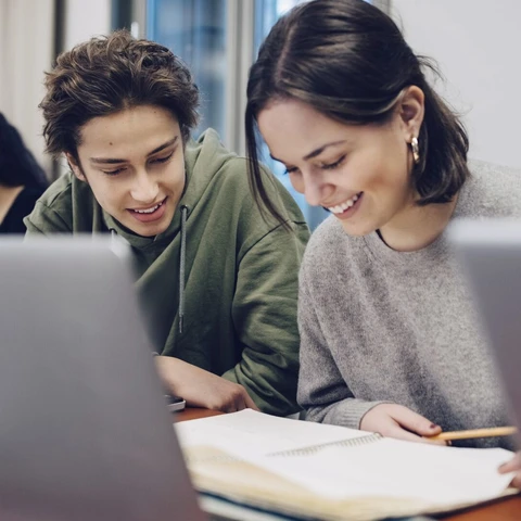 smiling-teenage-students-studying-at-desk-in-school