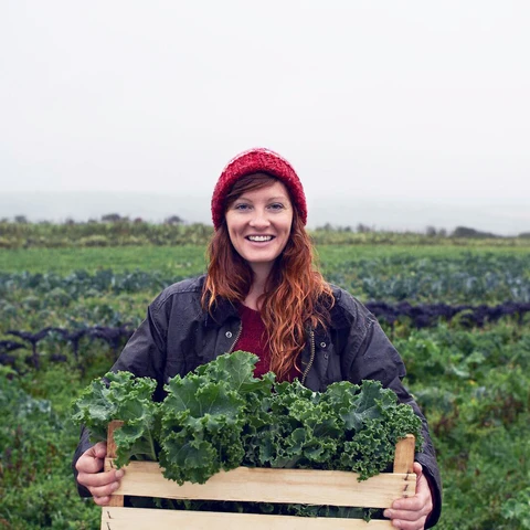 Smiling young woman holding greens on farm