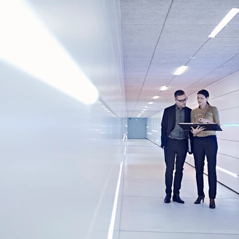 businesswoman-and-man-reading-file-in-office-corridor