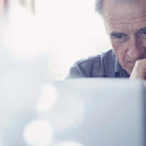 Senior man with hands clasped using laptop