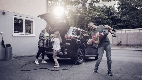Playful father and son with woman and girl standing by car in back yard_0.